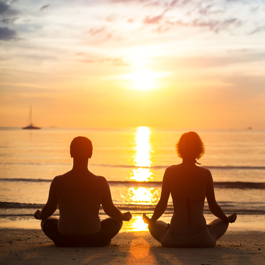 Yoga couple meditating on the sea beach.